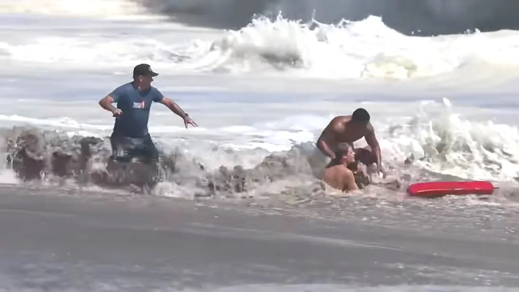 Lifeguard assisting a person struggling in rough ocean waves.