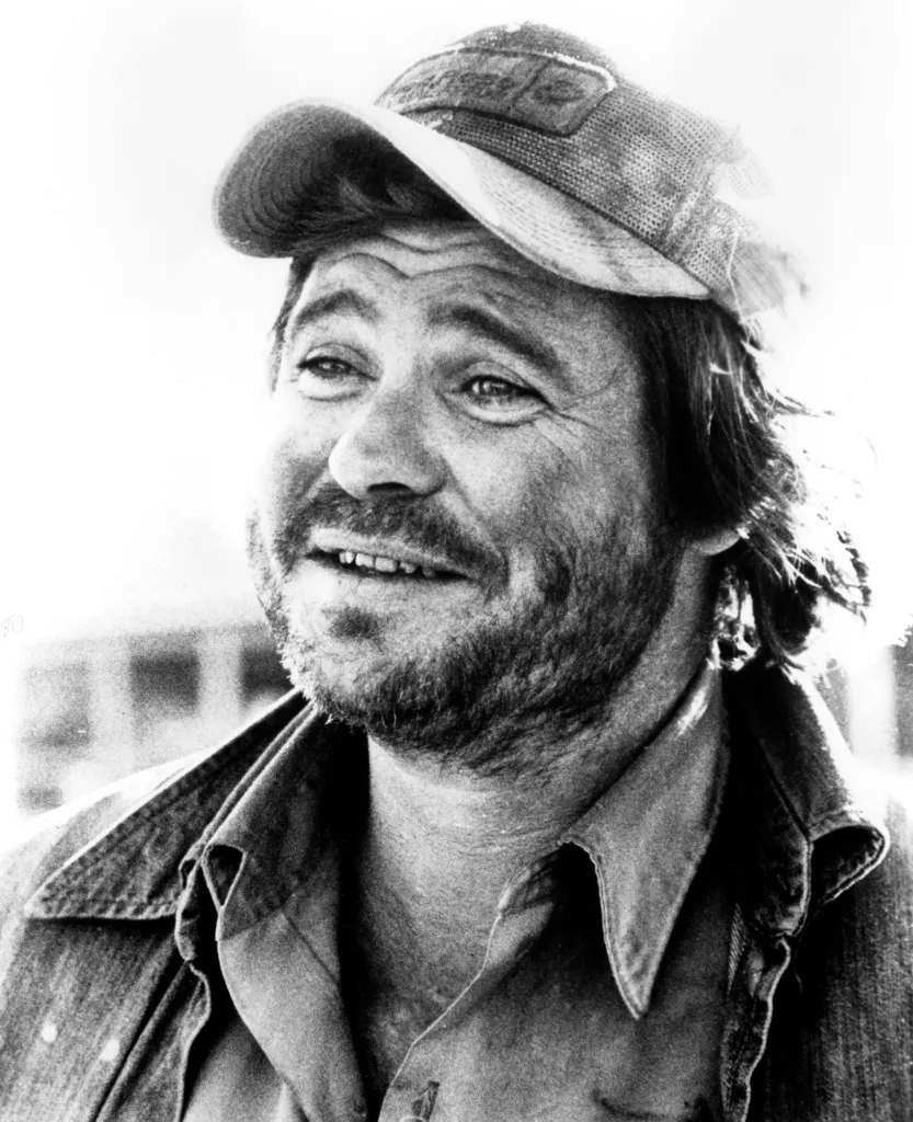 Ben Jones with an unshaven face, wearing a dirty baseball cap and a denim jacket.