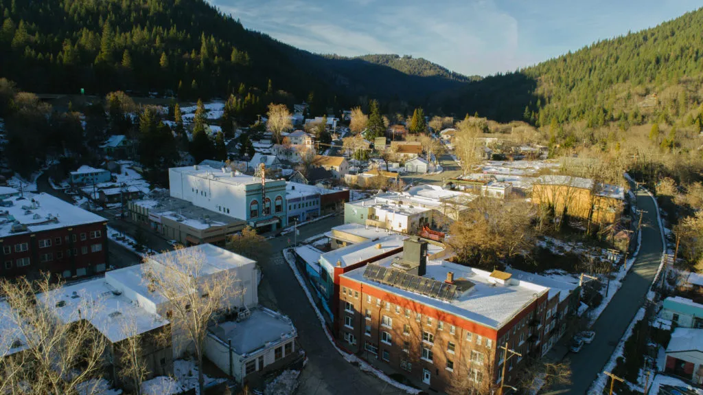 Aerial view of Dunsmuir's historic district with snow-dusted roofs and tree-covered mountains in the background.