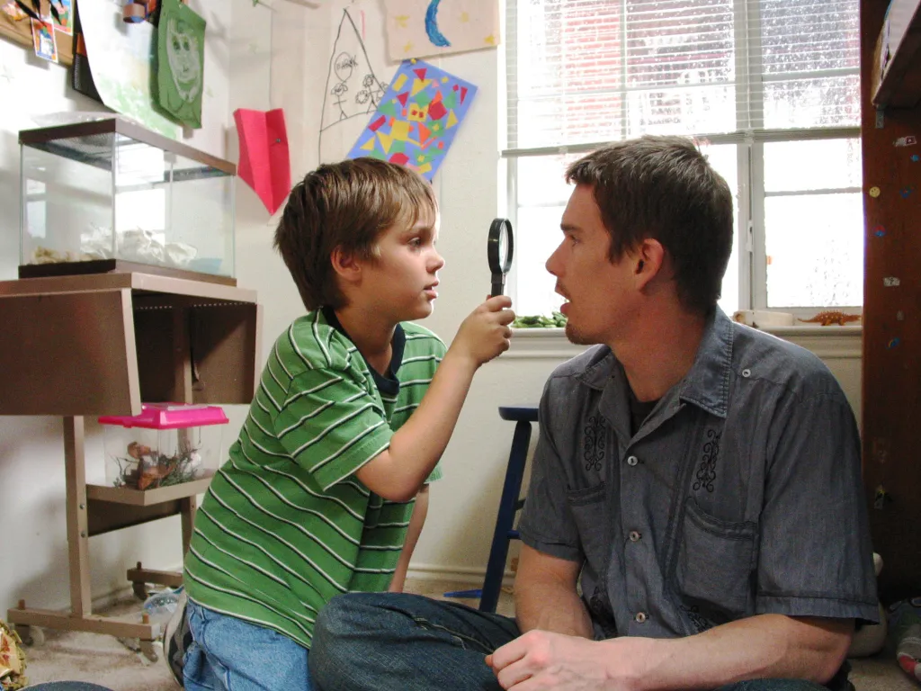 A boy in a green and white striped shirt holding a magnifying glass up to a man's face.