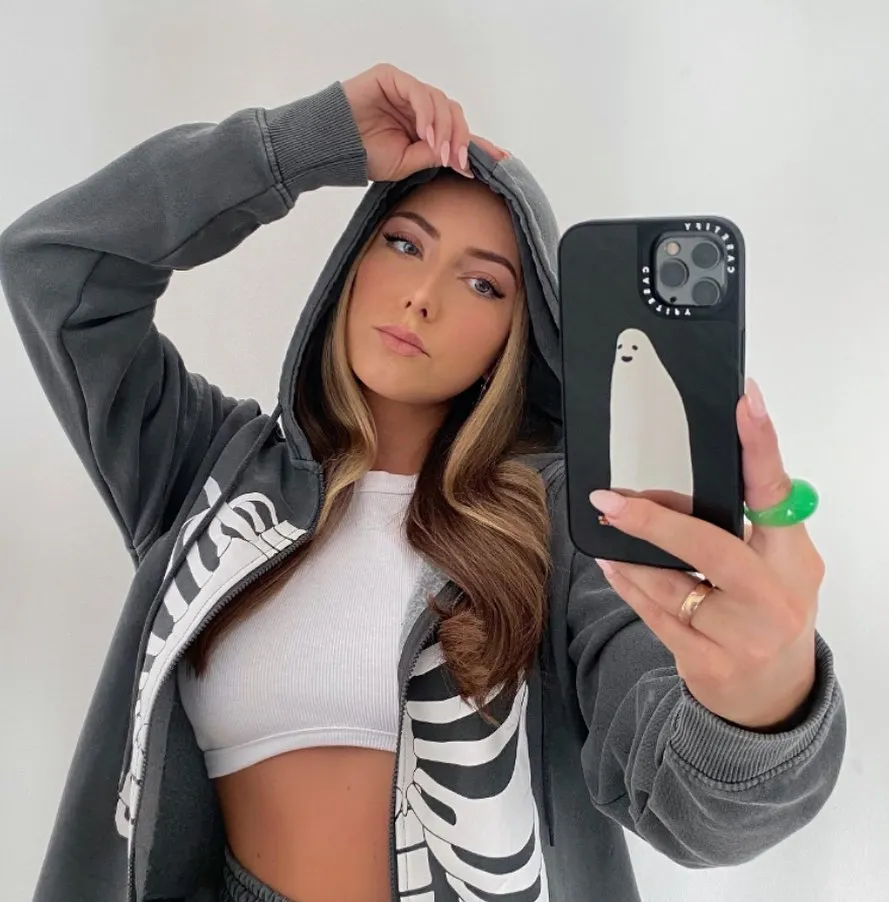 Hailie Jade wearing a skeleton hoodie and holding a phone with a ghost on the case.