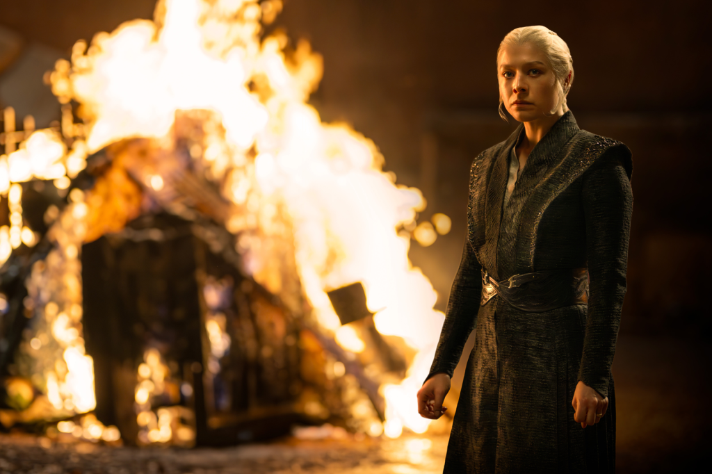 Emma D'Arcy as Rhaenyra Targaryen in House of the Dragon, standing in front of a burning pyre.