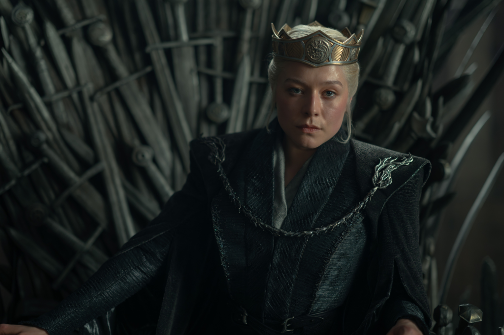 Emma D'Arcy as Rhaenyra Targaryen wearing a crown and dark attire on the Iron Throne.