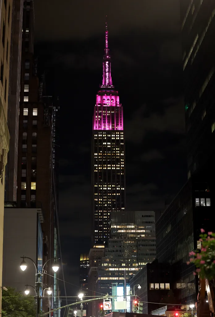The Empire State Building is lit up in pink at night.