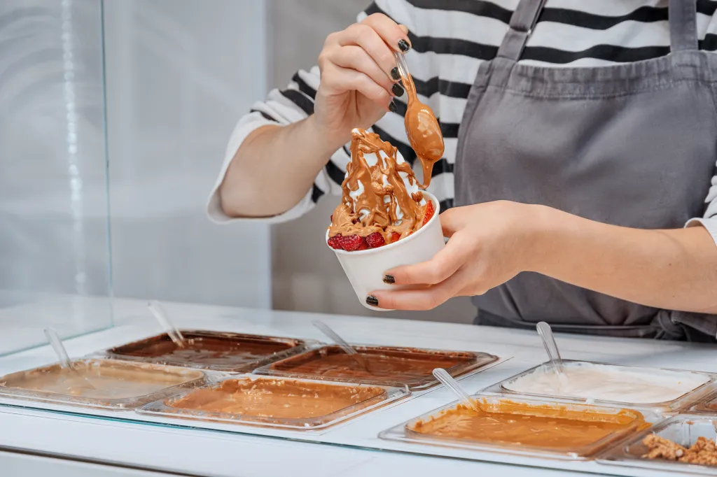 Employee adding melted chocolate sauce to a frozen yogurt cup with strawberries.
