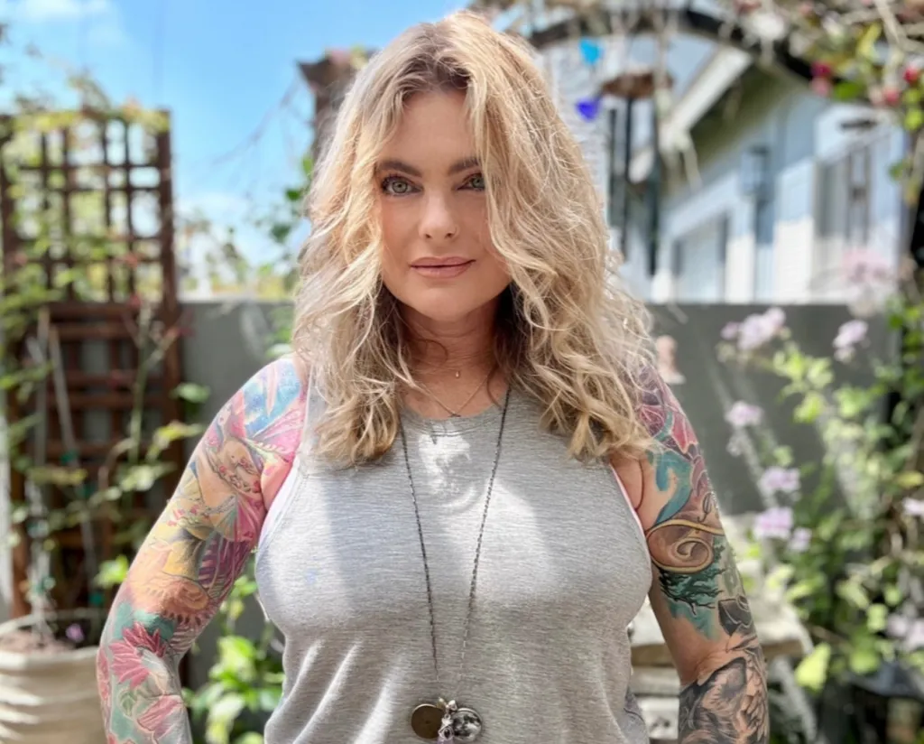 Erika Eleniak posing outdoors, showing her tattooed arms.