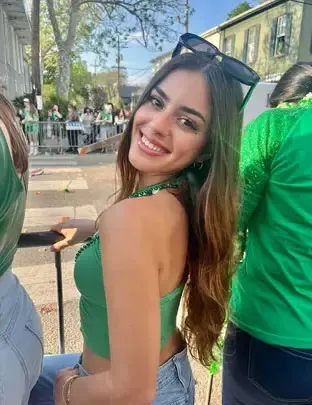 Lily Dalton, a woman with long brown hair and sunglasses on her head, smiles at the camera while wearing a green top.