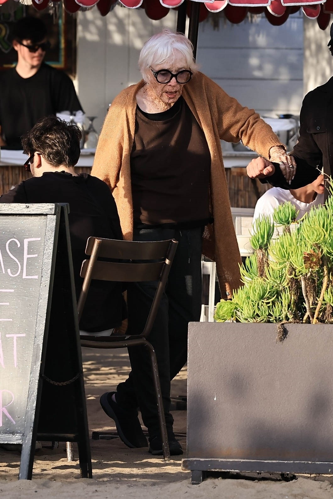 Shirley MacLaine being assisted while walking outside a restaurant.