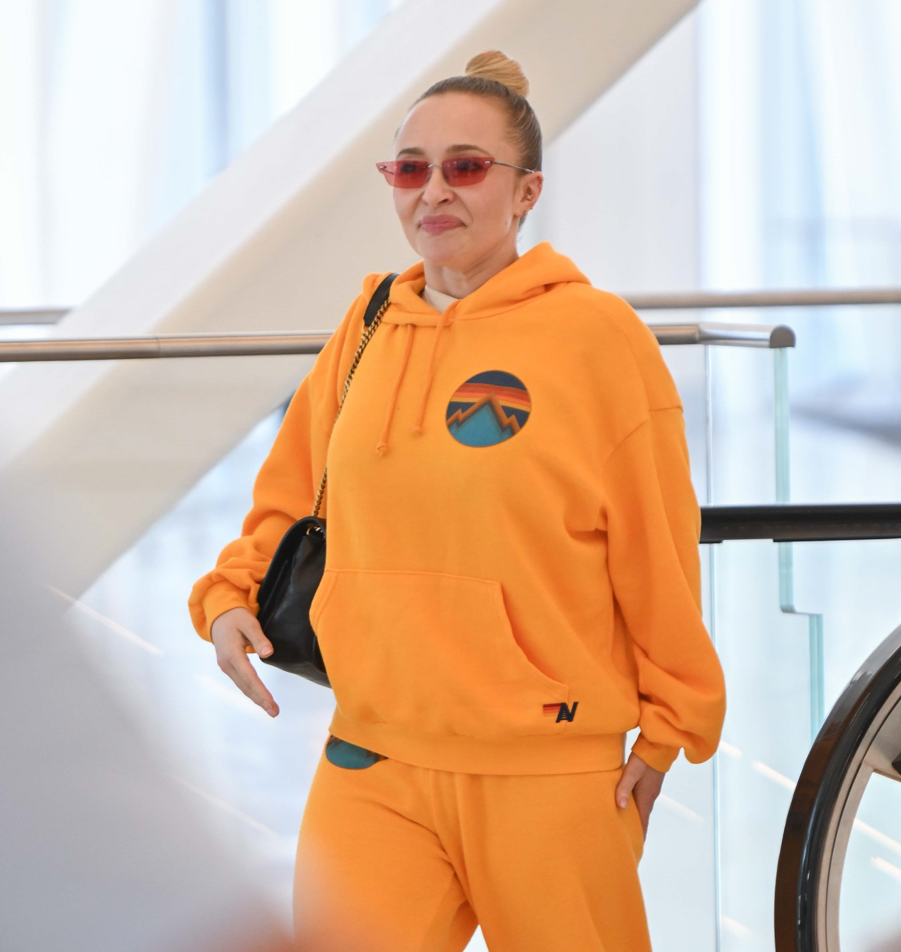 Hayden Panettiere wearing an orange sweatsuit and pink sunglasses at LaGuardia Airport.