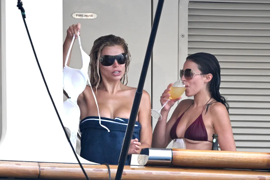 Brooks Nader in sunglasses holding a white bikini top, next to Sarah Jane Nader drinking from a glass.