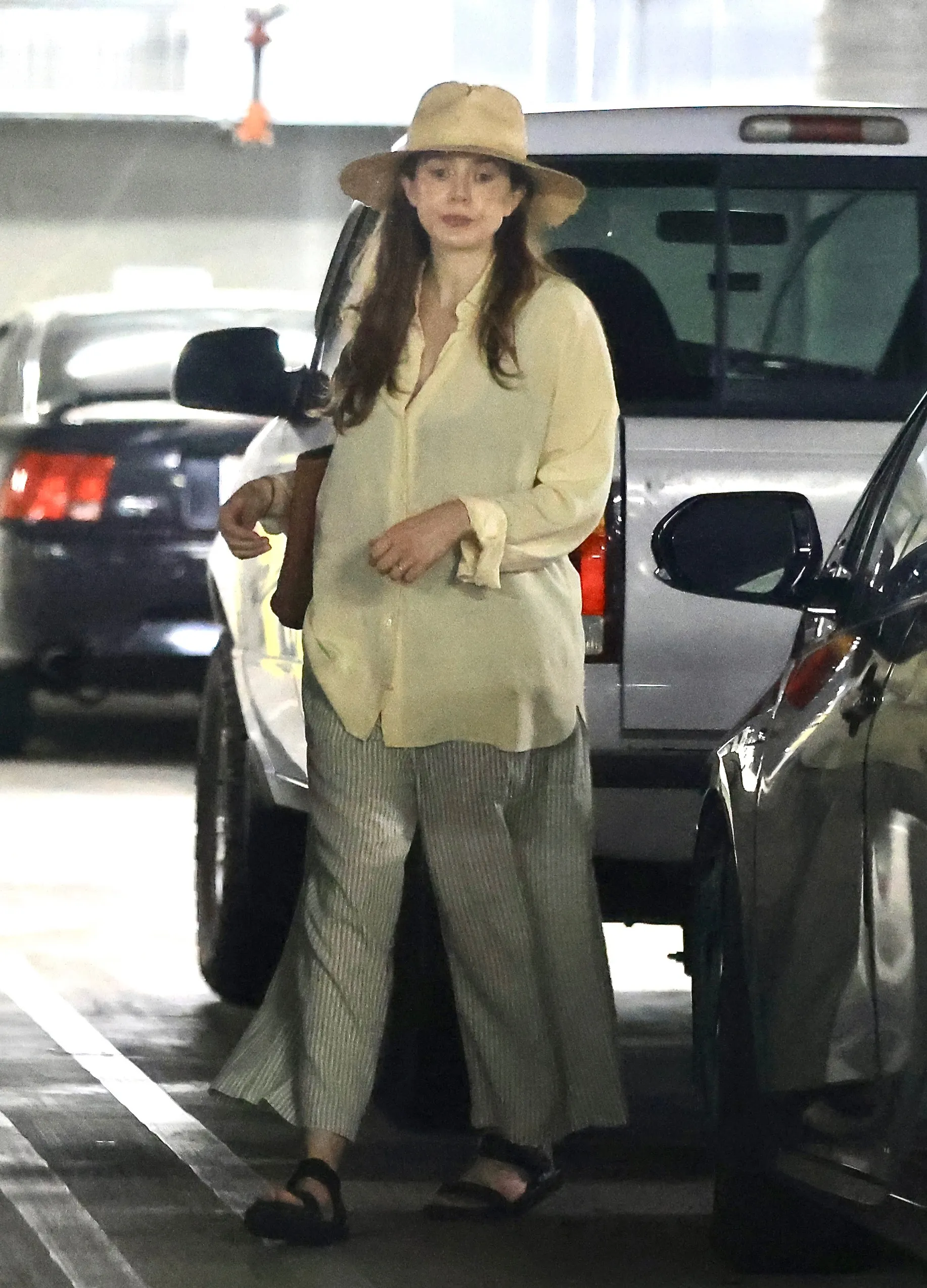 Elizabeth Olsen in a yellow blouse, pinstripe wide-leg pants, and black sandals, wearing a straw hat.