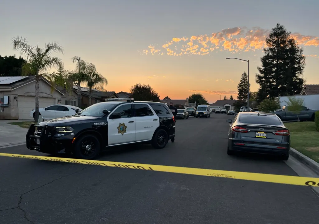 A Fresno police car parked on a residential street cordoned off with yellow tape, indicating a death investigation.