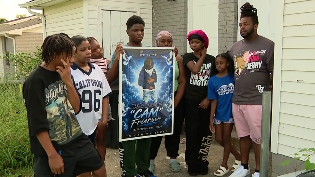 Family members stand together, holding a memorial poster for Cameron Frierson.