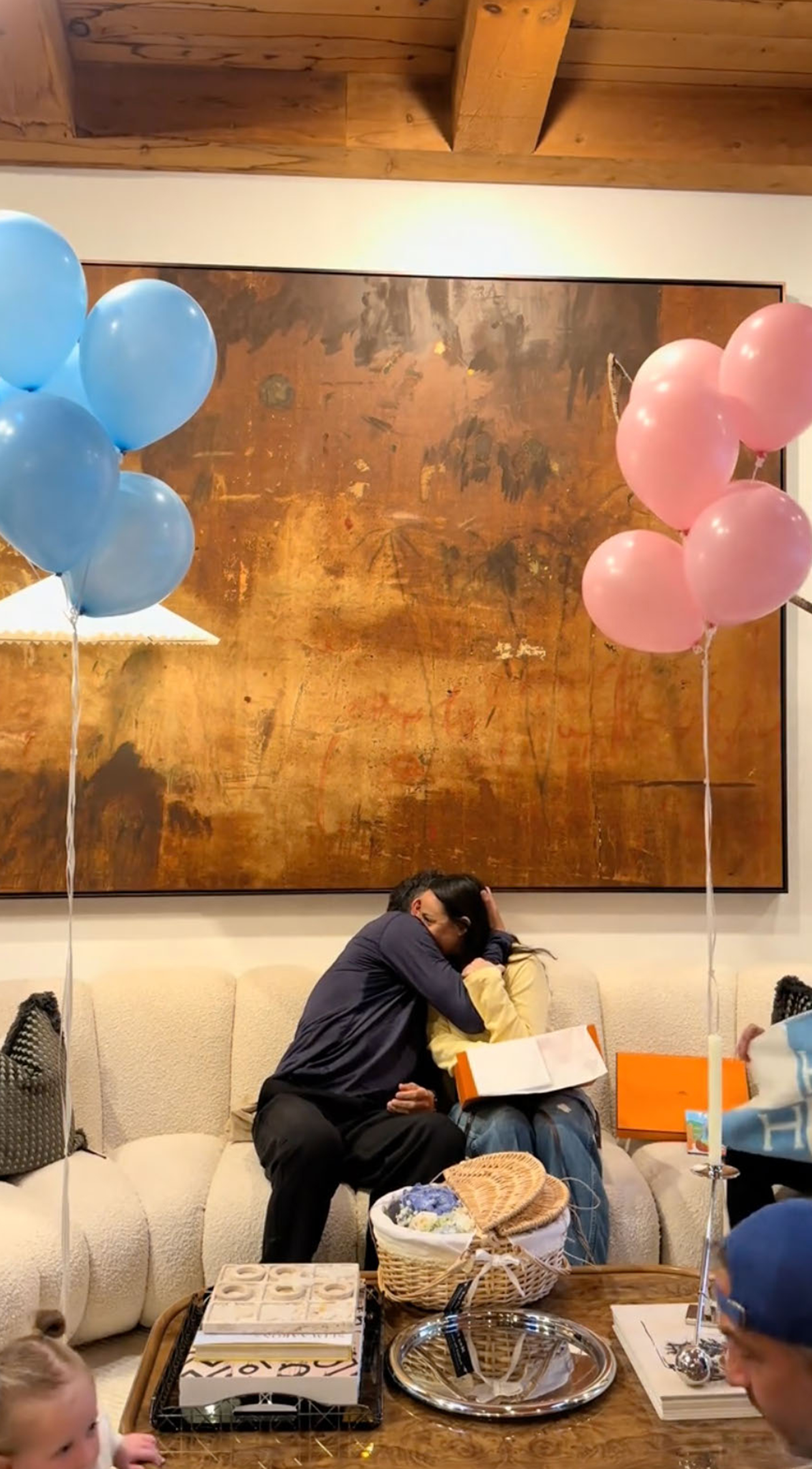 Farrah Brittany and Zach Goldsmith embrace on a couch with pink and blue balloons on either side.