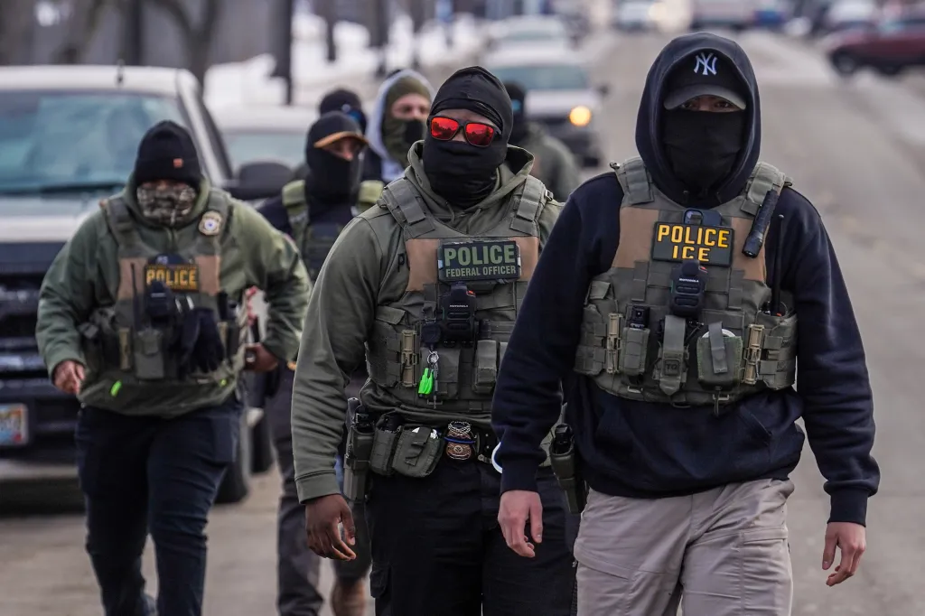 Federal agents walk down a street while conducting immigration enforcement operations.