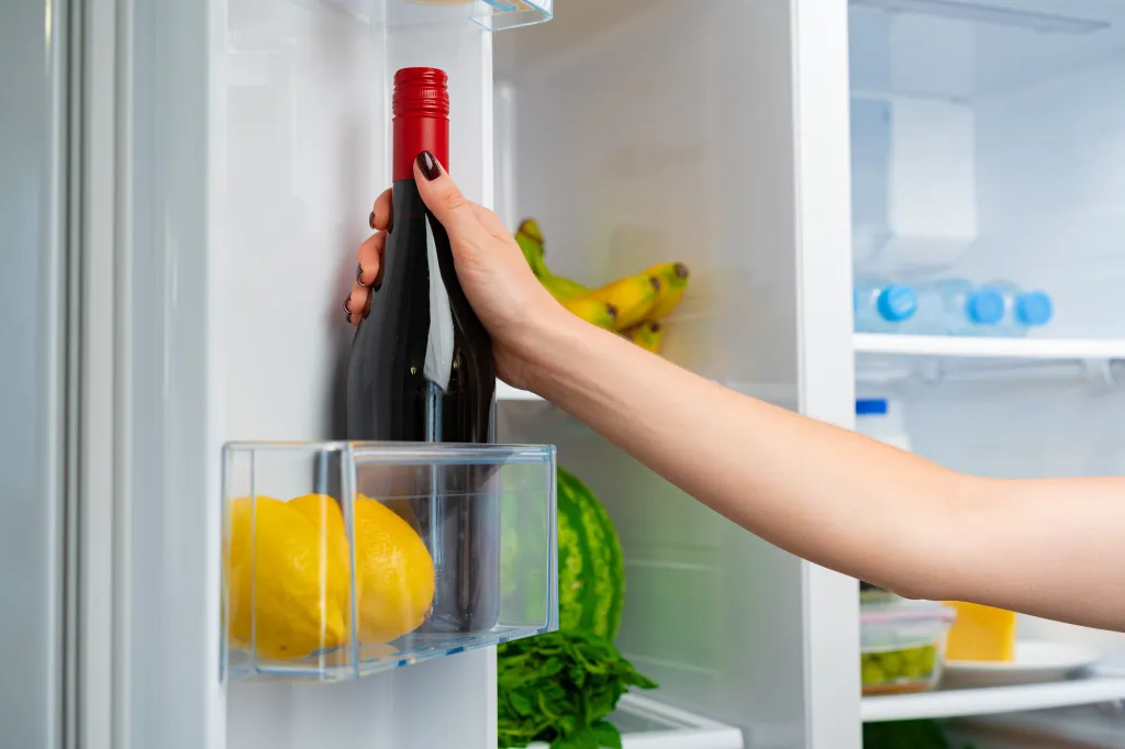 Female hand taking a bottle of wine from a fridge.