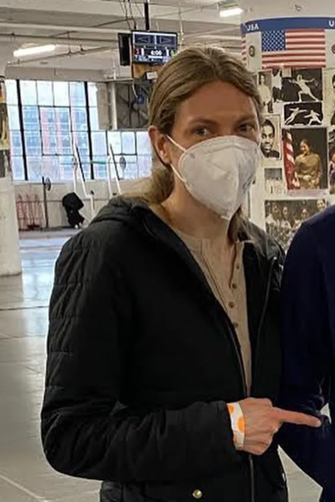 Fencing coach Lauren Phillips wearing a white mask and black jacket, pointing.
