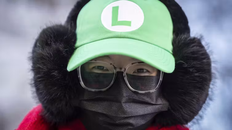 A supporter outside court wears eyeglasses, a black face mask and a green hat with an 'L' logo