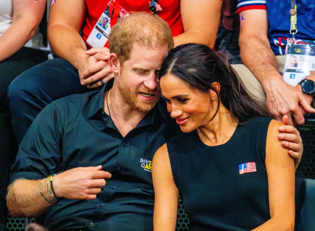 Meghan Markle and Prince Harry sitting closely together, smiling at an event.