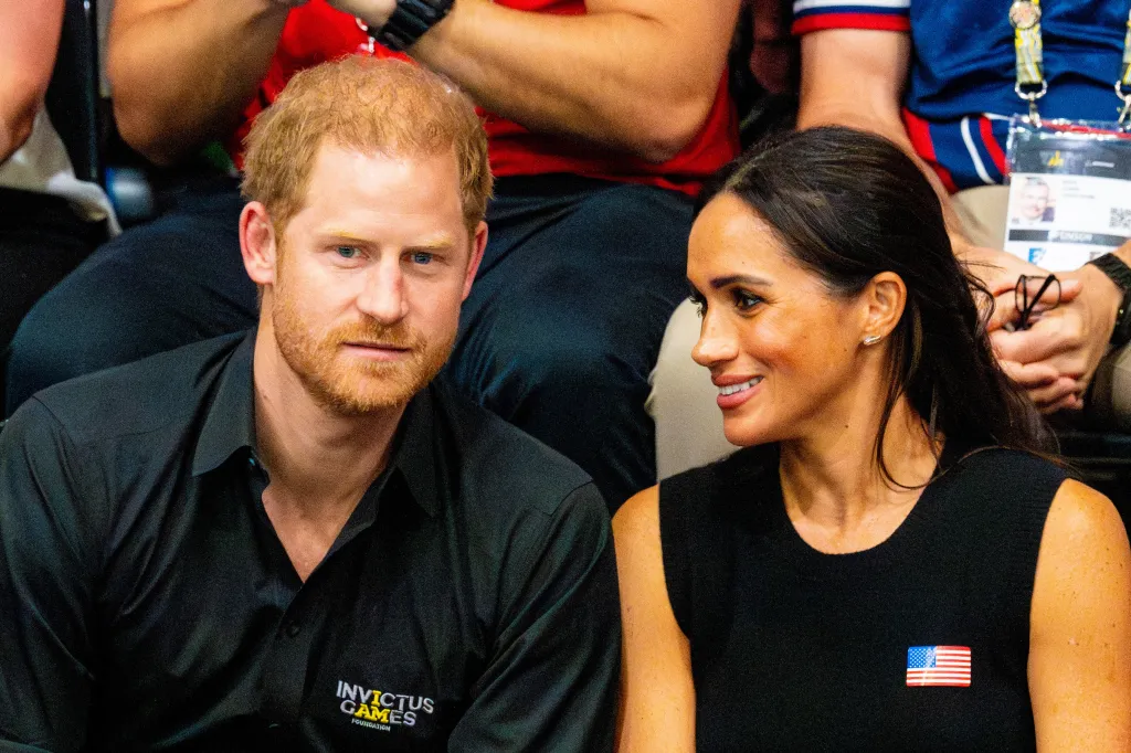 Prince Harry looking forward and Meghan Markle smiling while wearing an American flag pin.