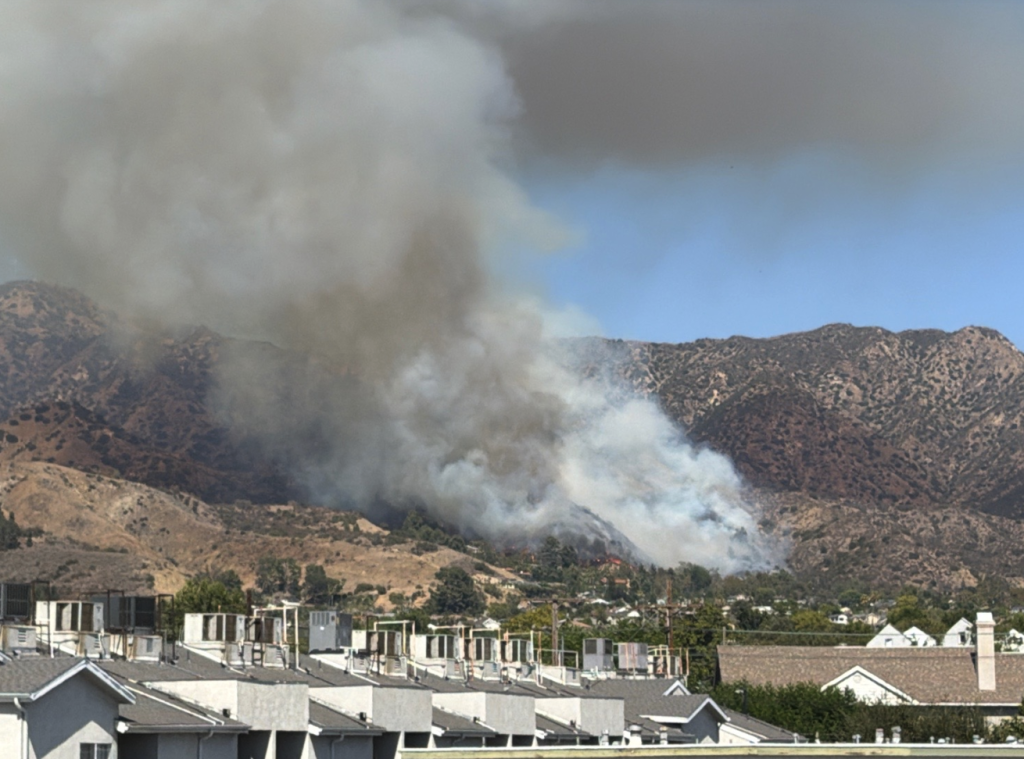 Smoke from the Walnut Fire rising above a hillside in Burbank, with residential rooftops visible in the foreground.