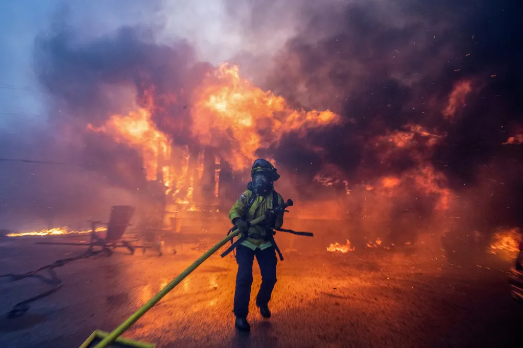 A firefighter battling the Palisades Fire, surrounded by flames and smoke during a windstorm in Los Angeles.