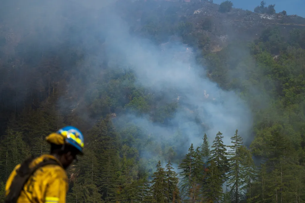A firefighter in the foreground looks over Castro Canyon as the Timber Fire burns in Big Sur, California, producing thick smoke among the trees.
