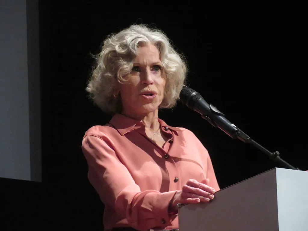 Jane Fonda speaking at a podium with a microphone.