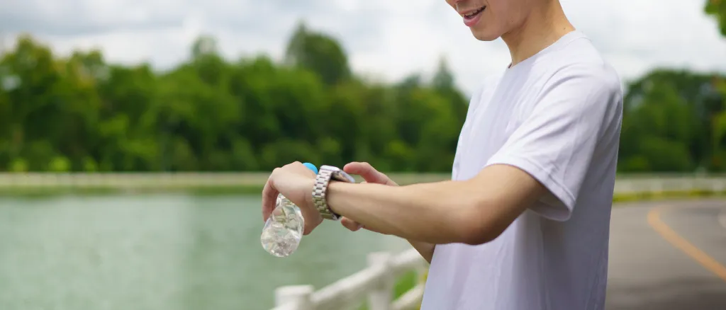 A man in a white t-shirt checks his smartwatch while holding a water bottle.