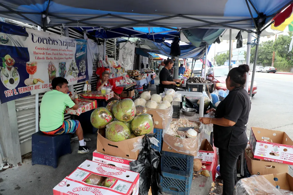 Food vendors under tents selling coconuts and other goods on Salvador Corridor in Los Angeles.