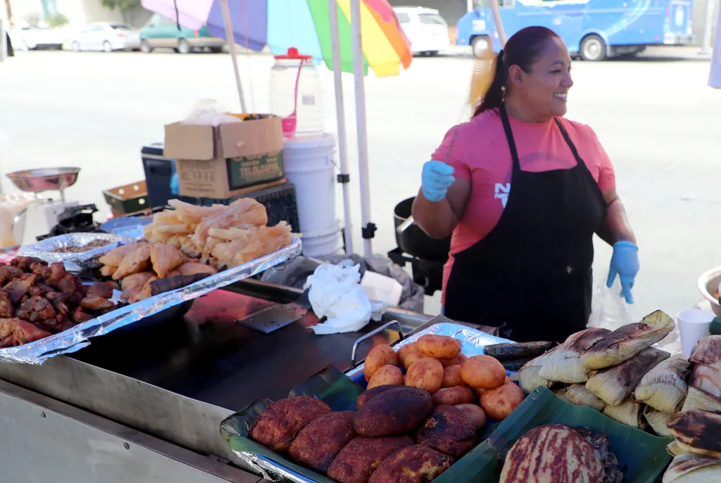 Food vendor at the Salvador Corridor, Los Angeles, selling various foods including fried meats and tamales.