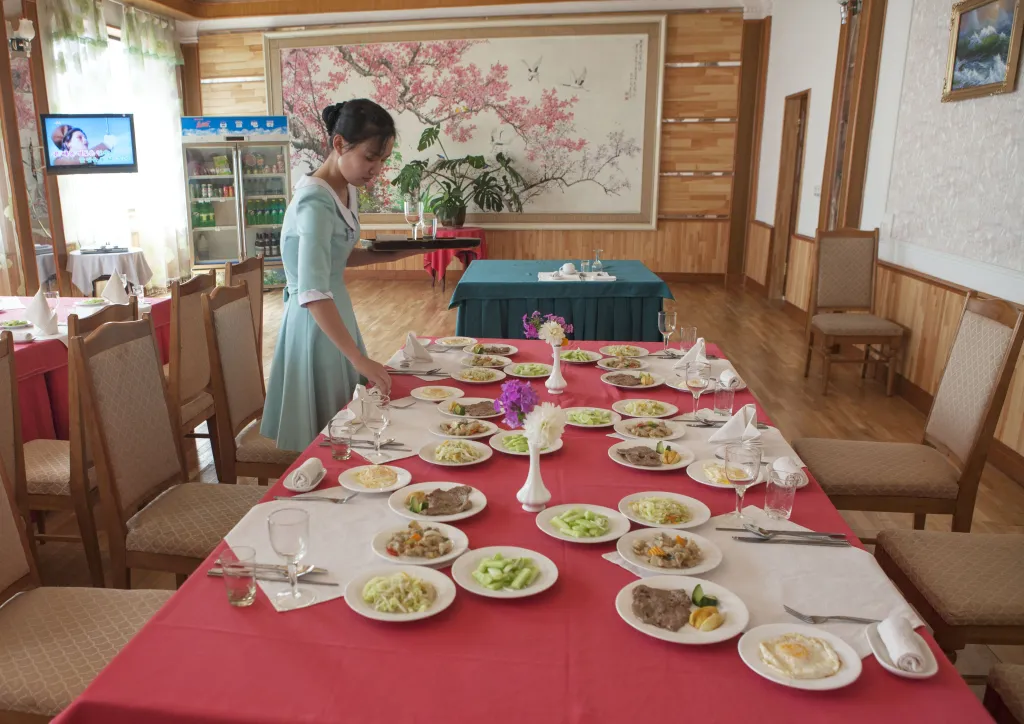 A server placing a tray on a large table laden with individual plates of food for tourists in a restaurant in Hamhung, North Korea.