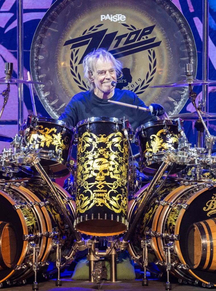 Frank Beard of ZZ Top performing on drums with a large gong behind him.