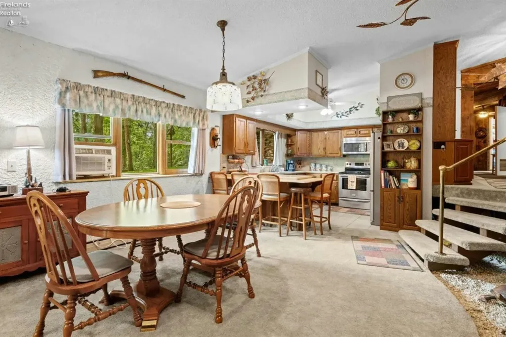 Dining area with a round wooden table and chairs, adjacent to a kitchen with wooden cabinets and stainless steel appliances.