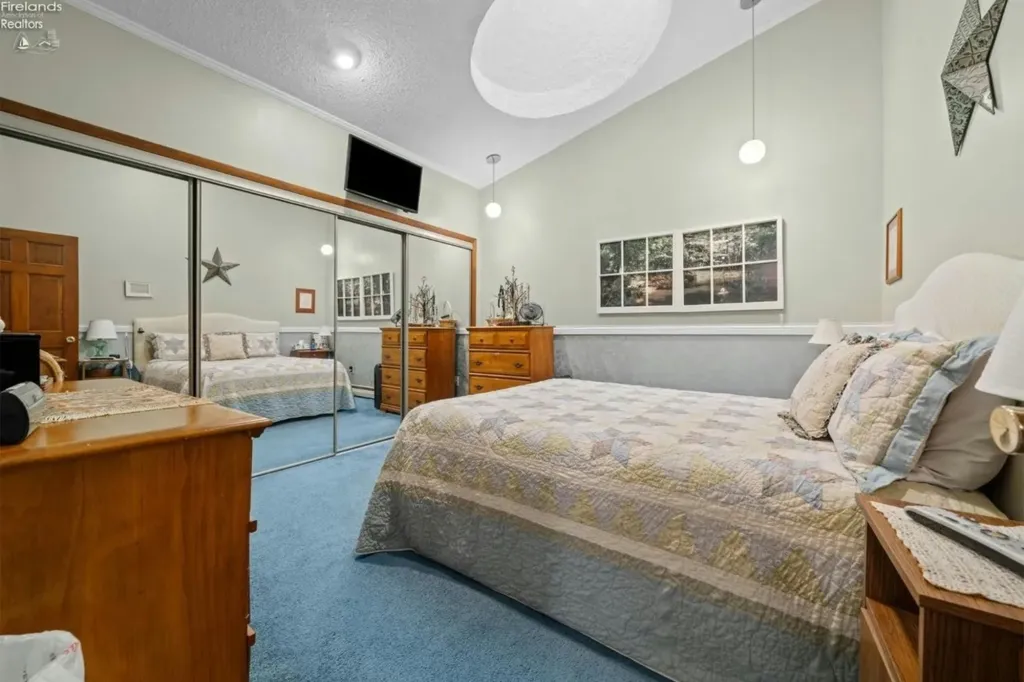 Bedroom with blue carpet, a bed with a patterned quilt, and mirrored closet doors.