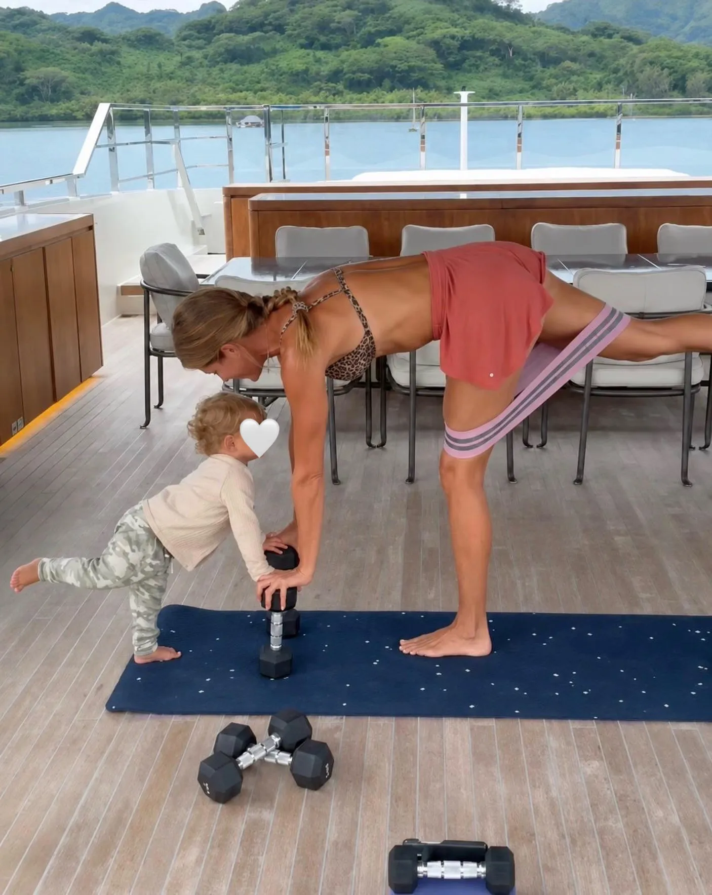 Gisele Bundchen exercising on a yacht with her child holding a dumbbell.