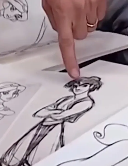 A person's finger points at a sketch of a character.