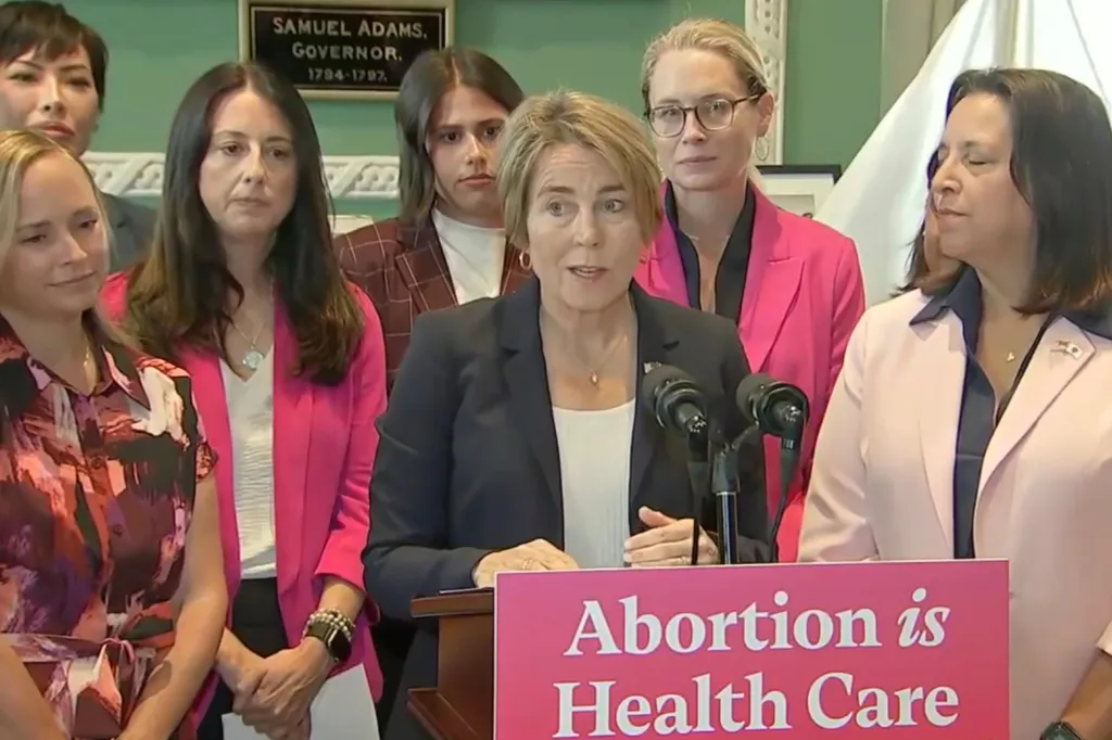 Massachusetts Governor Maura Healey speaks at a podium with the sign