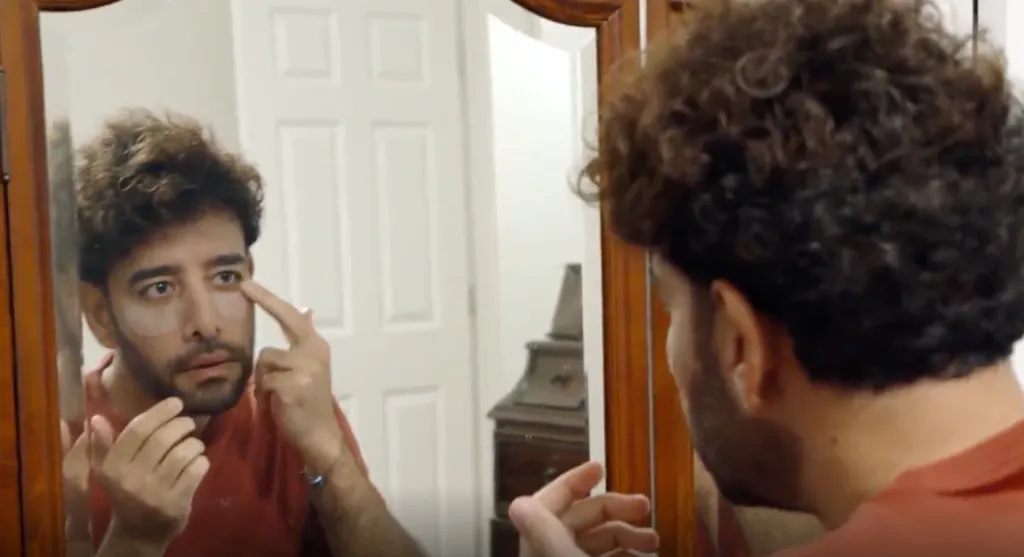 Man applying under-eye patches in a mirror.