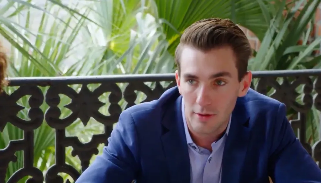 Julian from 90 Day Fiance in a blue suit jacket and light blue shirt sitting on a patio.