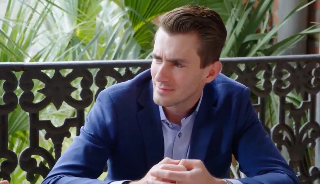 A man in a blue suit looks to his right, smiling subtly.