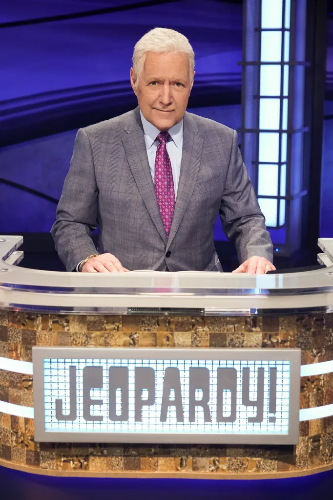Alex Trebek stands behind a podium with the