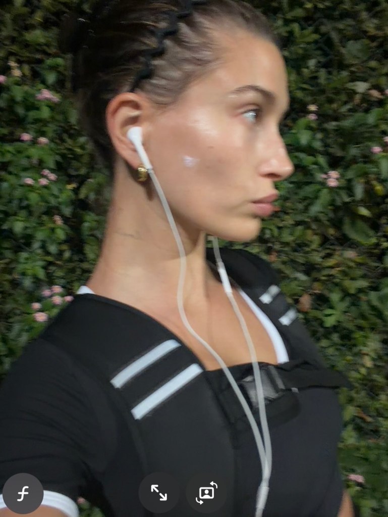 Hailey Bieber wearing earphones, black activewear, and a braided headband.