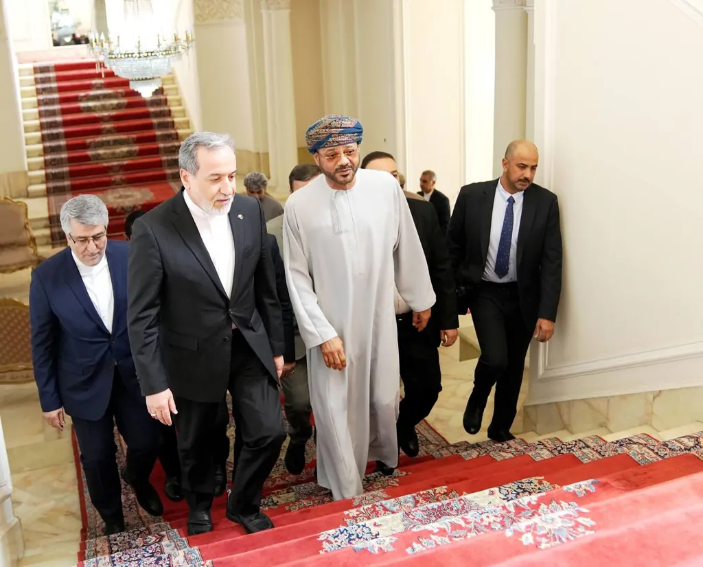 Iranian Foreign Minister Abbas Araghchi and Omani Foreign Minister Sayyid Badr Al Busaidi walk together up a grand staircase in Tehran.
