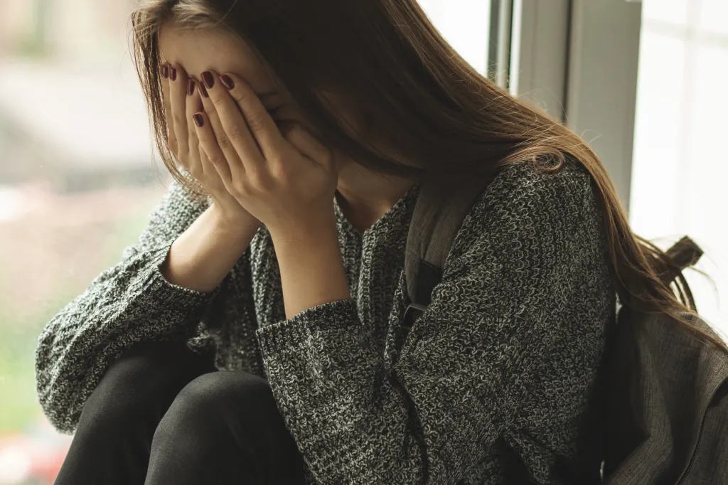 A young woman sitting, covering her face with her hands, appearing upset.