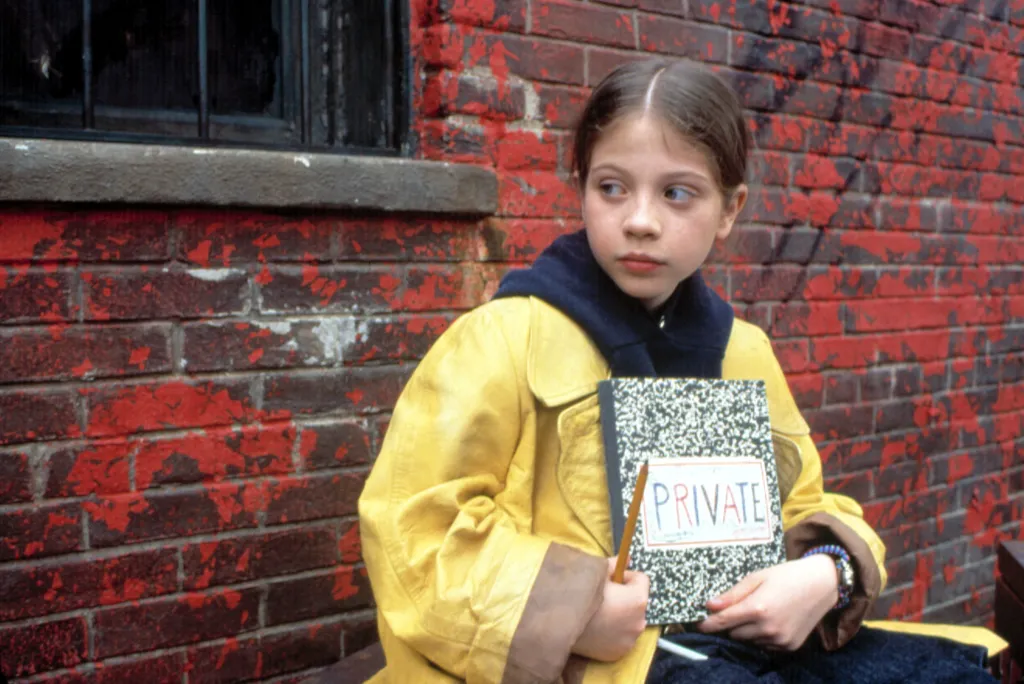 Michelle Trachtenberg as Harriet the Spy, wearing a yellow raincoat and holding a notebook with 