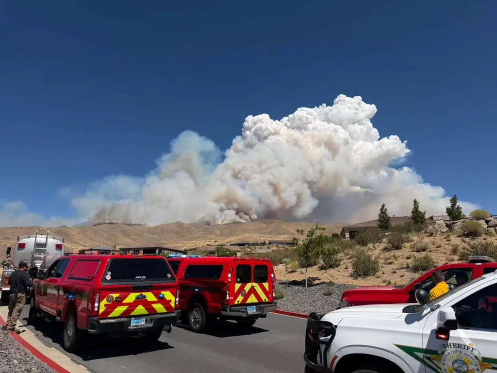 Firefighting vehicles and a sheriff's truck with a large plume of smoke from the Hawk Fire rising in the background.