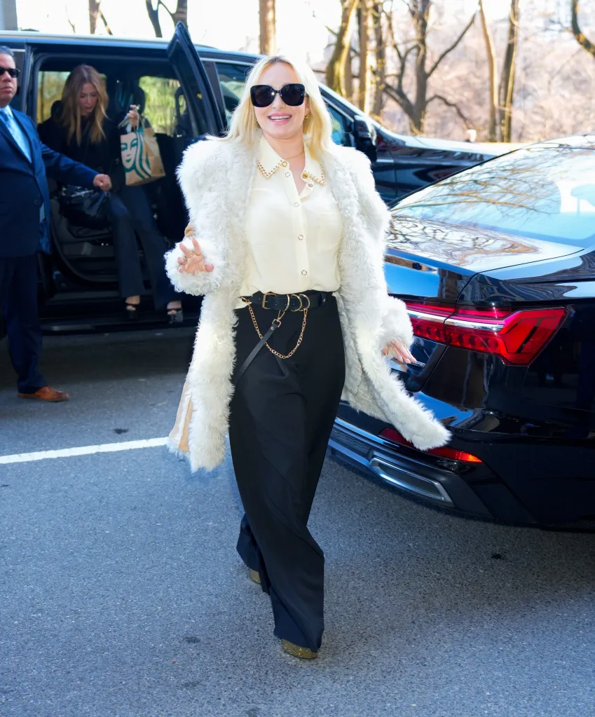 Hayden Panettiere wearing sunglasses, a white fur coat, and black pants, walking away from an open car door.