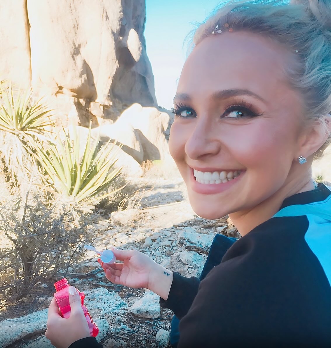 Hayden Panettiere smiling and holding a bubble wand and bottle.