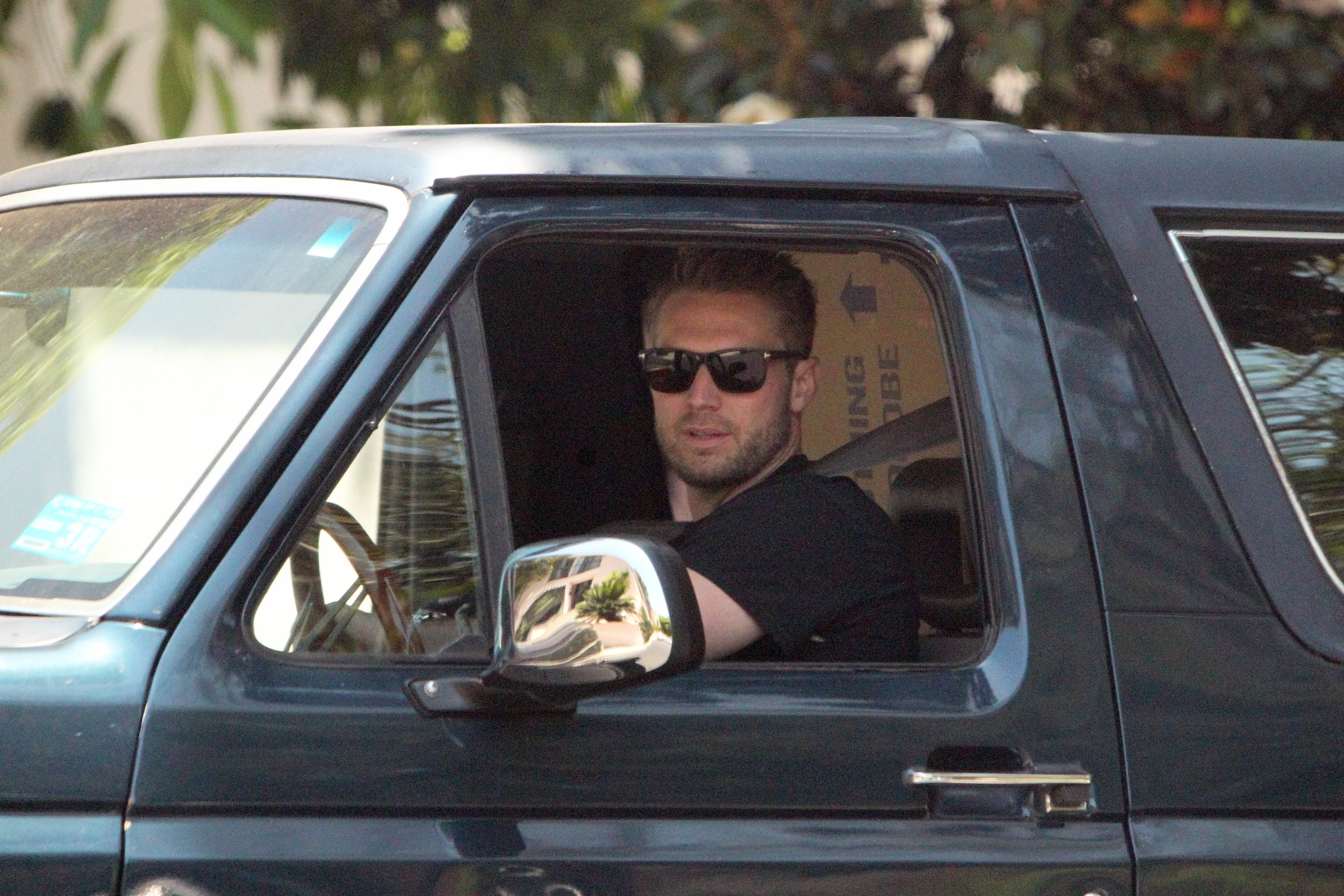 Brian Hickerson in sunglasses, driving a Bronco with boxes in the back.